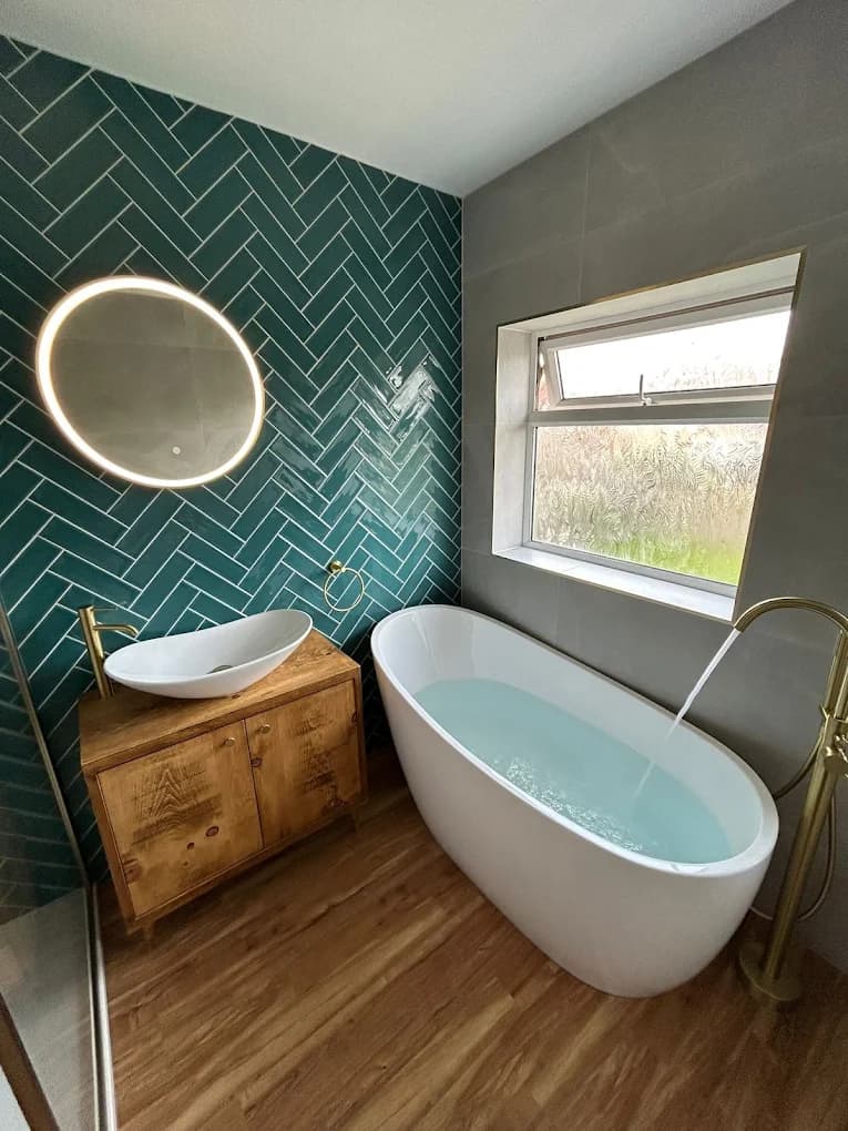 Round backlit mirror on the teal herringbone wall beside the window