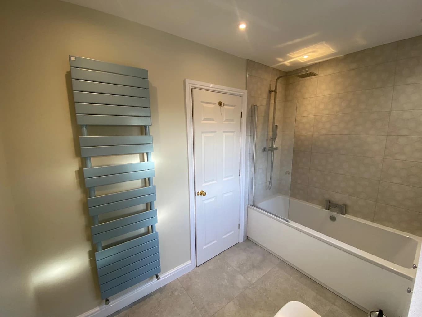 Teal designer radiator beside a bath with cream walls and a glass shower screen