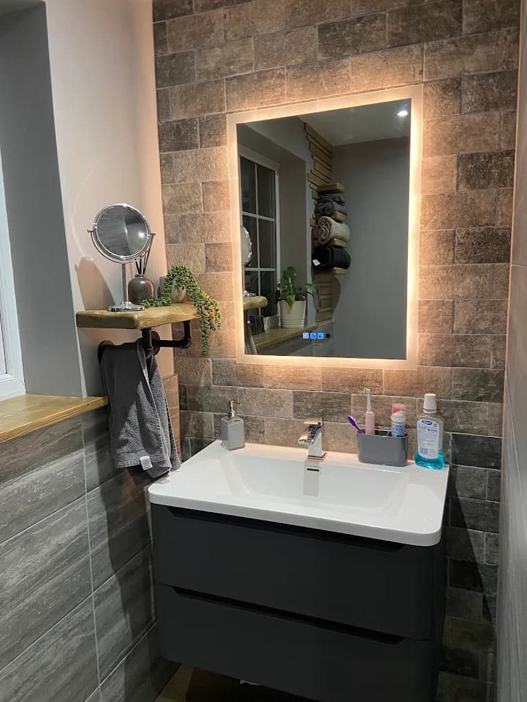 Walnut-topped vanity under a backlit mirror in a dark tiled bathroom