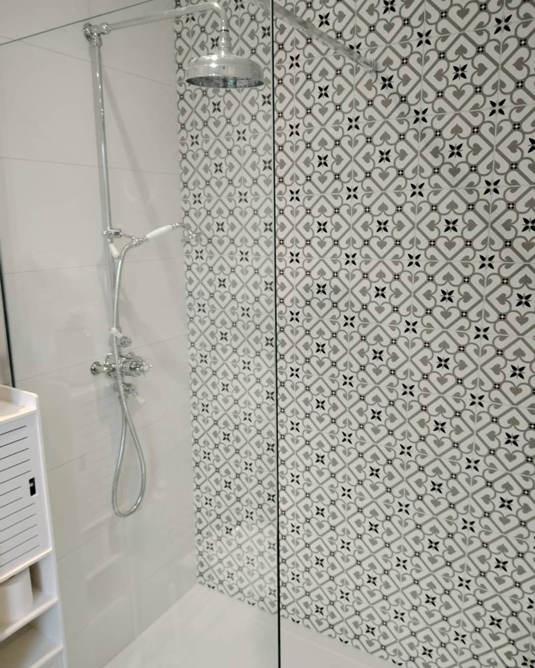 Walk in shower with monochrome patterned wall tiles, a chrome exposed riser with a rain head and handset, and a glass screen