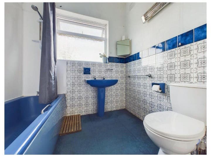Dated bathroom with a blue bath, blue pedestal basin and blue and white patterned wall tiles