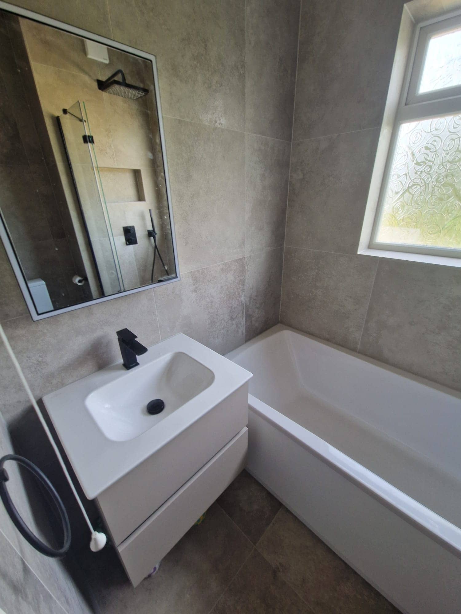 Wall hung vanity unit with a black tap and a black framed mirror, next to the bath
