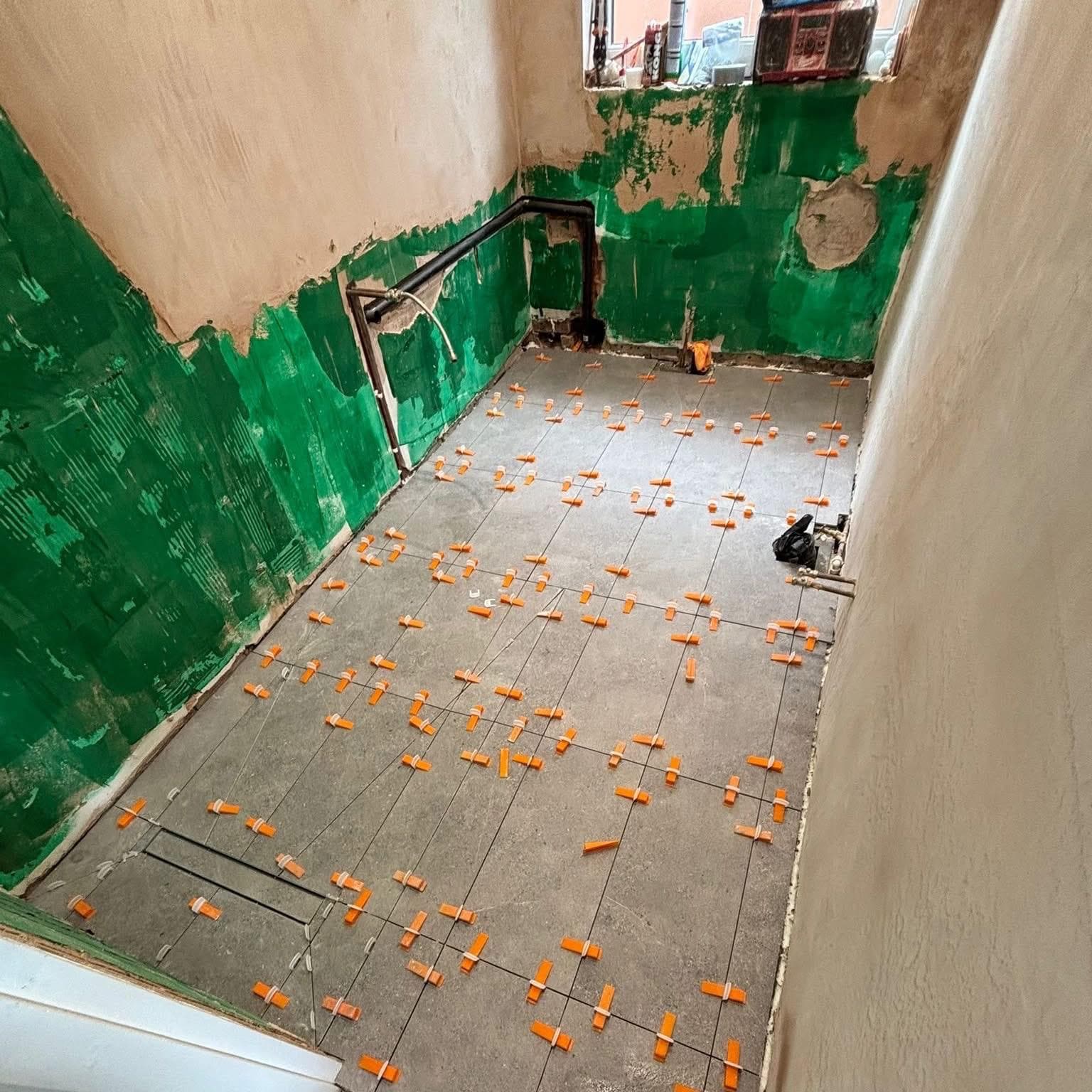 Bathroom mid renovation with floor tiles laid under levelling clips and green waterproofing on the lower walls